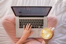 Blog - Laptop Screen - Coffee in hand - sitting on bed -